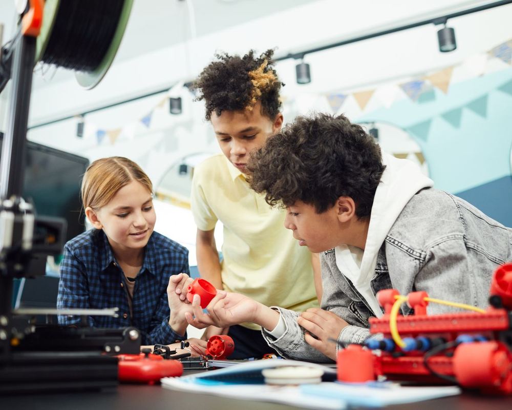 Three children building a small red robot together at a table