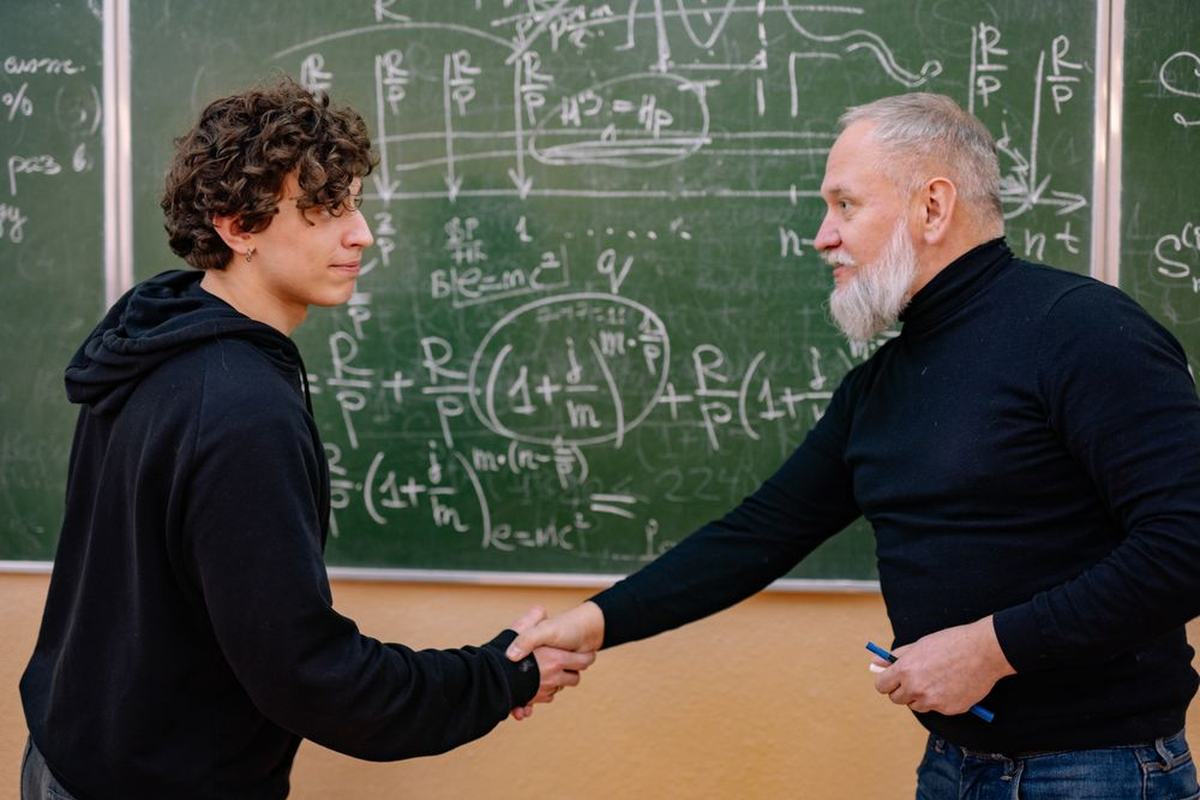 A teacher and a student shaking hands in front of a chalkboard