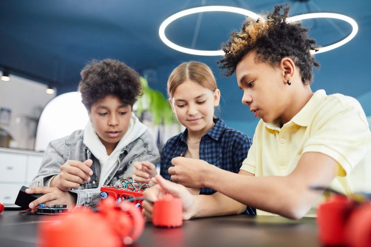 Three students building and testing a small red robot together at a table